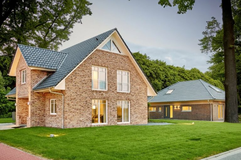 Massivhaus mit Klinkerfassade, Satteldach und seitlichem Bungalow-Anbau bei Abenddämmerung – Beispielobjekt für den Vergleich Massivhaus Fertighaus inkl. Preise